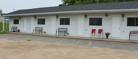 A motel with numbered doors, outdoor seating, and a parking lot.