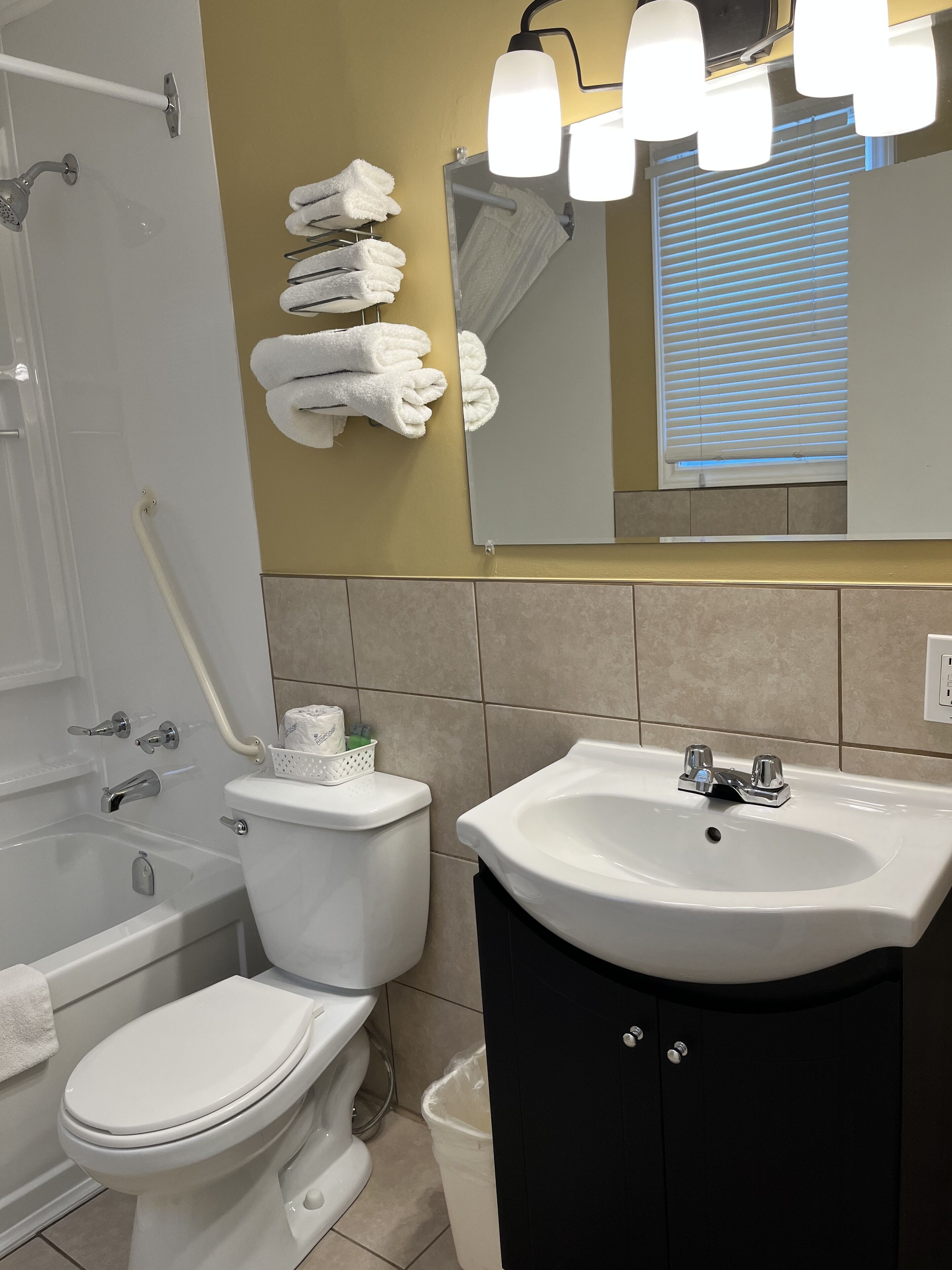 Ein Badezimmer mit Toilette, Waschbecken und Badewanne. Handtücher hängen an der Wand, und über dem Waschbecken hängt ein Spiegel.