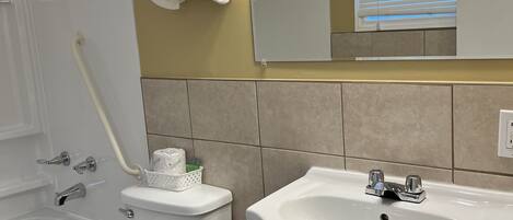 Ein Badezimmer mit Toilette, Waschbecken und Badewanne. Handtücher hängen an der Wand, und über dem Waschbecken hängt ein Spiegel.