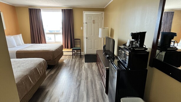 A hotel room with two beds, a desk with a coffee maker, a trash bin, and a door. - Travellers Inn Pembroke (Pembroke)