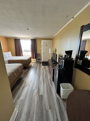 A hotel room with two beds, a desk with a coffee maker, a trash bin, and a door. - Travellers Inn Pembroke (Pembroke)