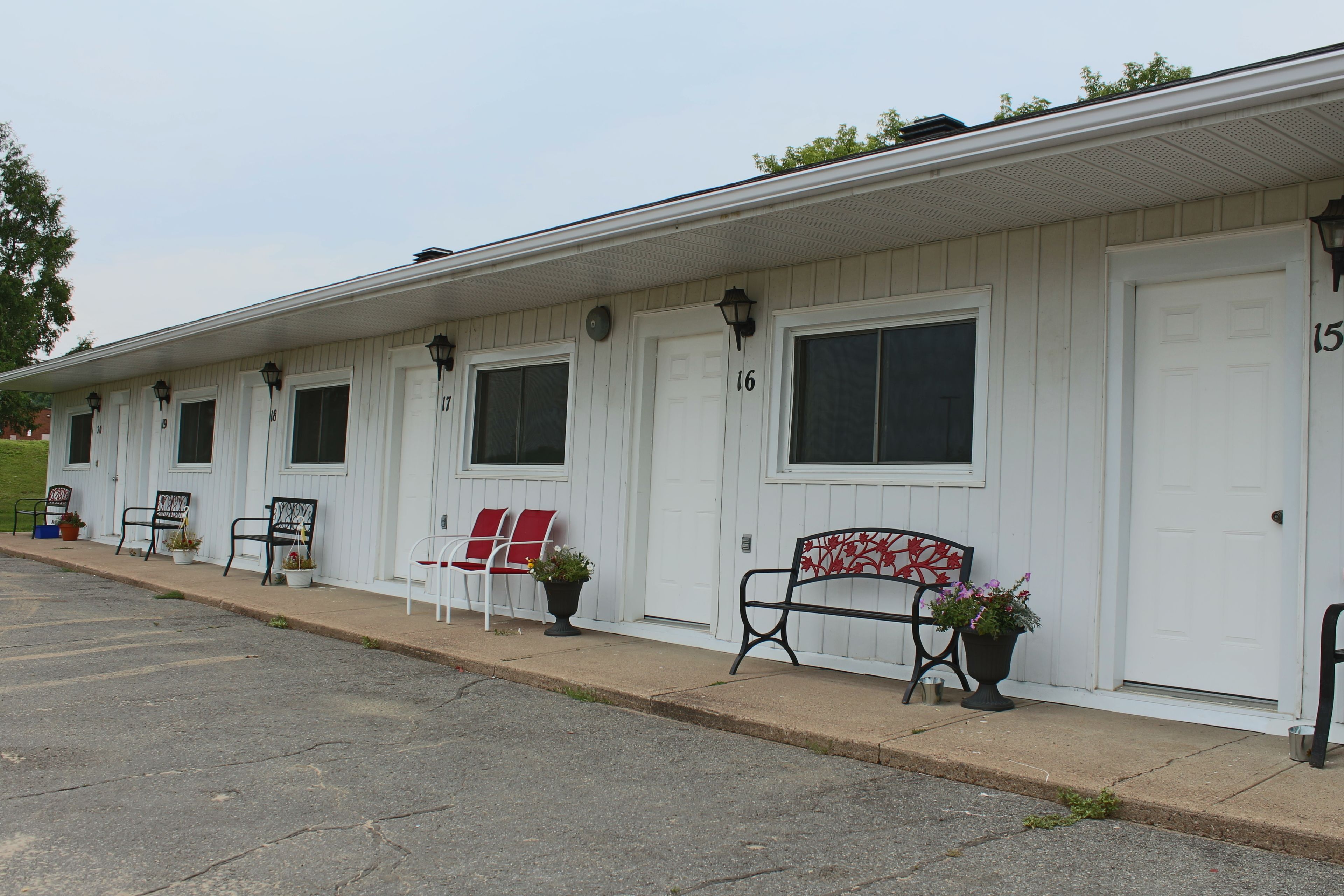 A row of white motel rooms with numbered doors, outdoor seating, and potted plants.