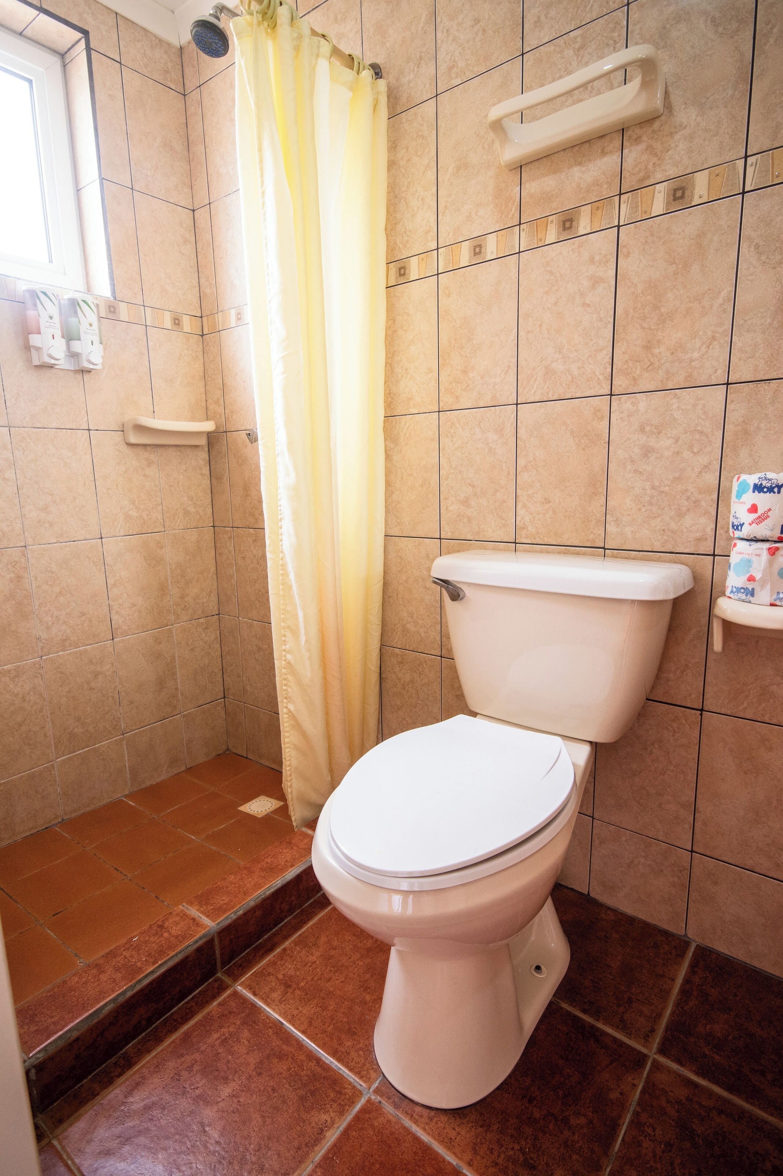 A bathroom with a toilet, shower curtain, and tiled walls.