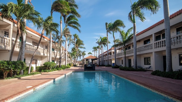 Una piscina rodeada de palmeras y un edificio con balcones.