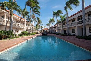 A swimming pool surrounded by palm trees and a building with balconies.