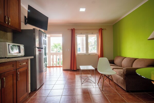 A compact living space with a kitchenette, a flat-screen TV, a dining area with a table and chairs, and a sofa.