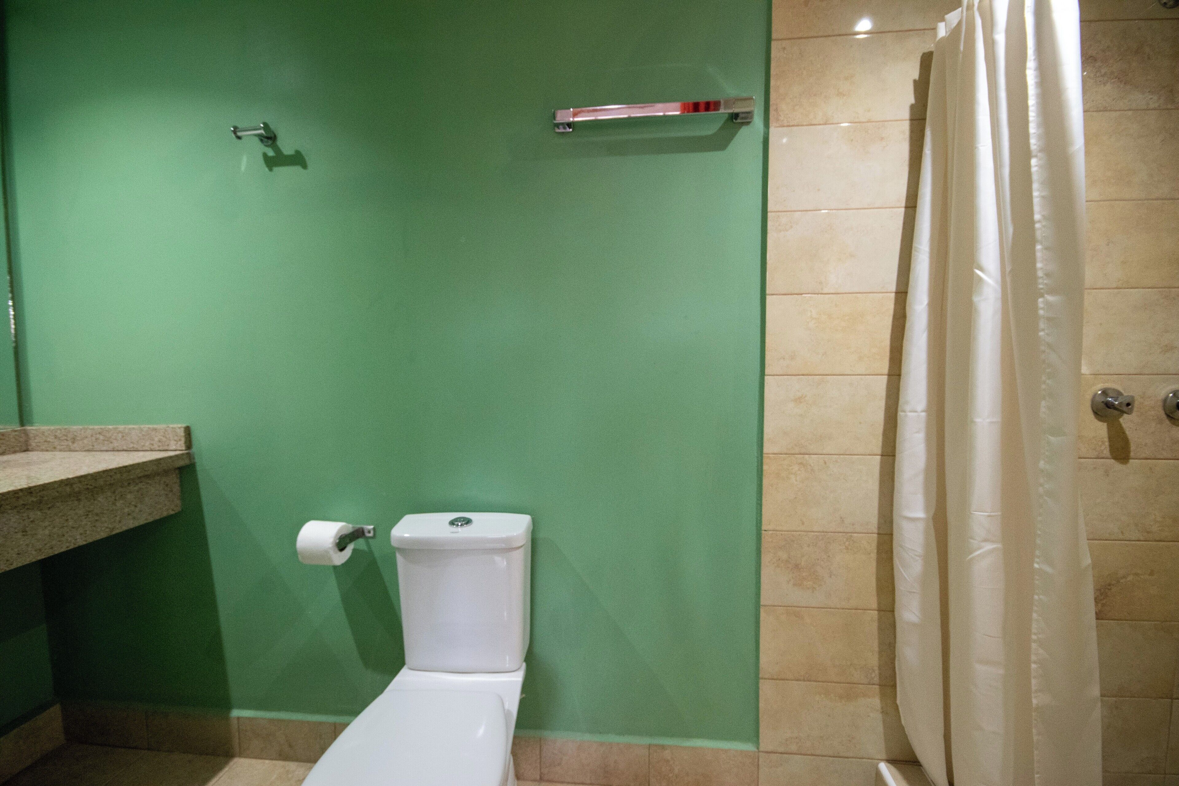 A bathroom with a green wall, a white toilet, a beige shower curtain, and a beige tiled floor.
