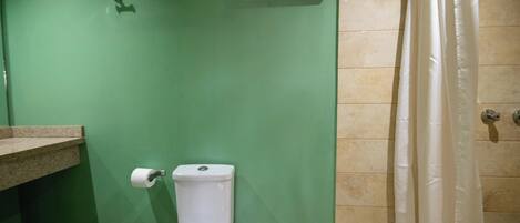 A bathroom with a green wall, a white toilet, a beige shower curtain, and a beige tiled floor.