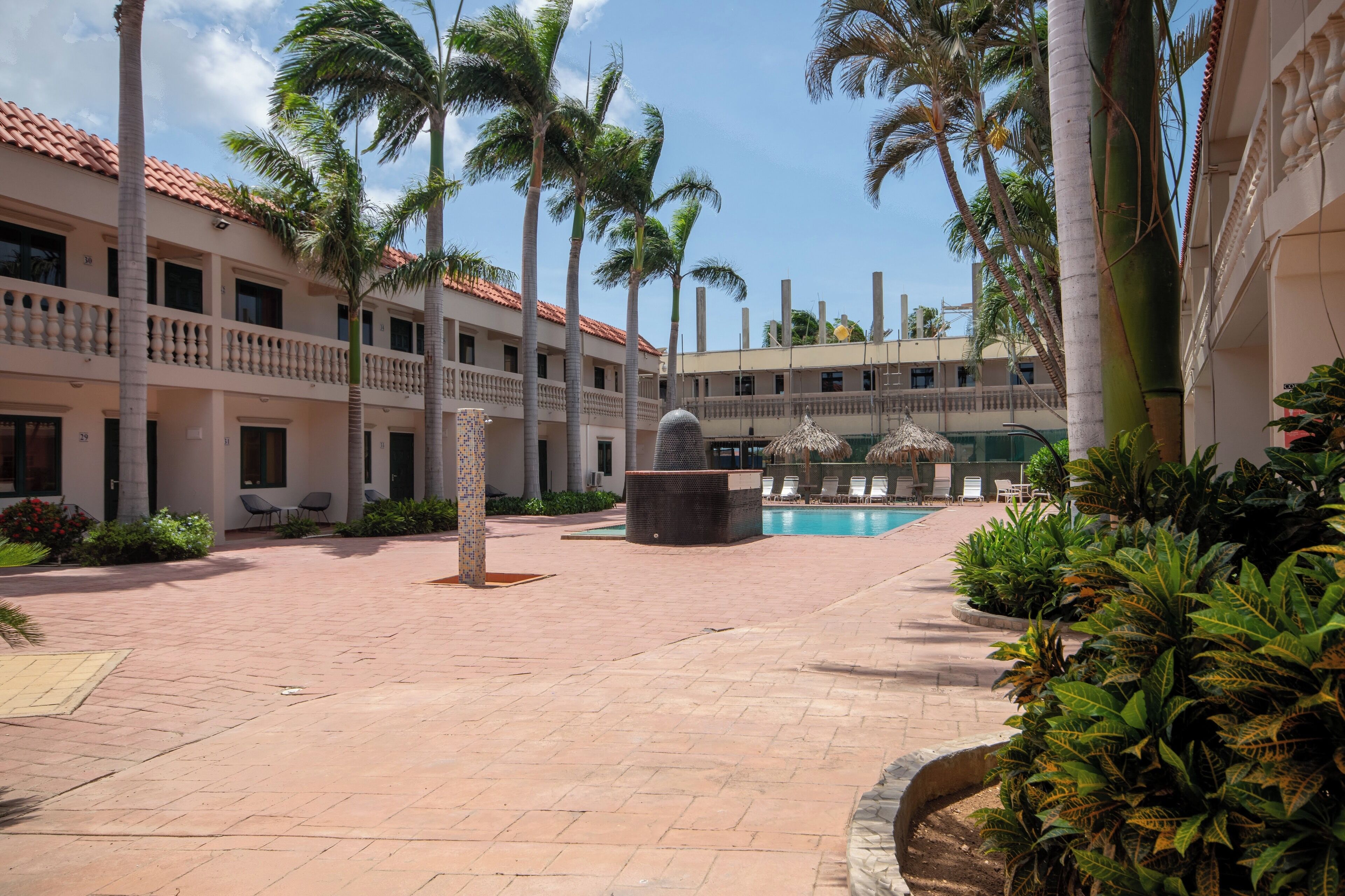 A courtyard with a pool, palm trees, and a building with balconies.
