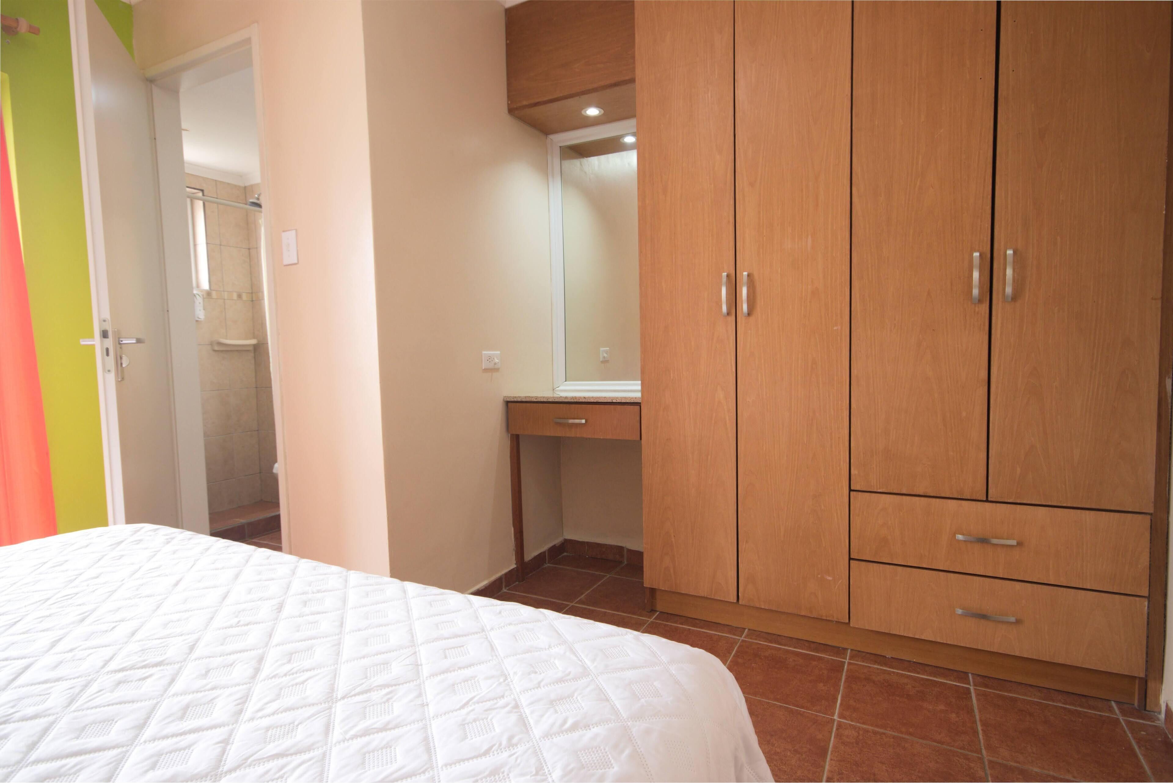 A bedroom with a bed, wooden wardrobe, and a bathroom visible through an open door.