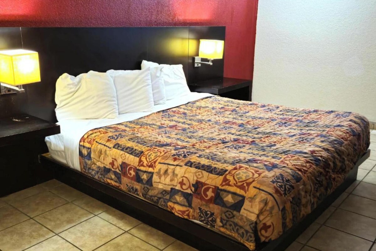 A hotel room with a bed, two bedside lamps, a headboard, and a nightstand.