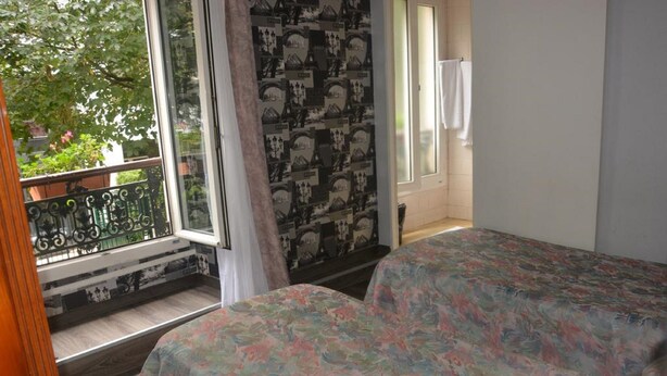 A bedroom with a bed, a window with a view of greenery, and a patterned wall. - Palace Hotel (Paris)