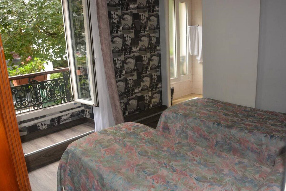 A bedroom with a bed, a window with a view of greenery, and a patterned wall.