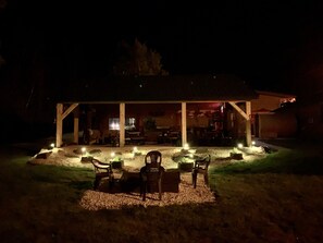 A covered outdoor seating area with chairs and tables, illuminated by ground lights, and a building in the background. - Whitetail Creek Resort (Lead)