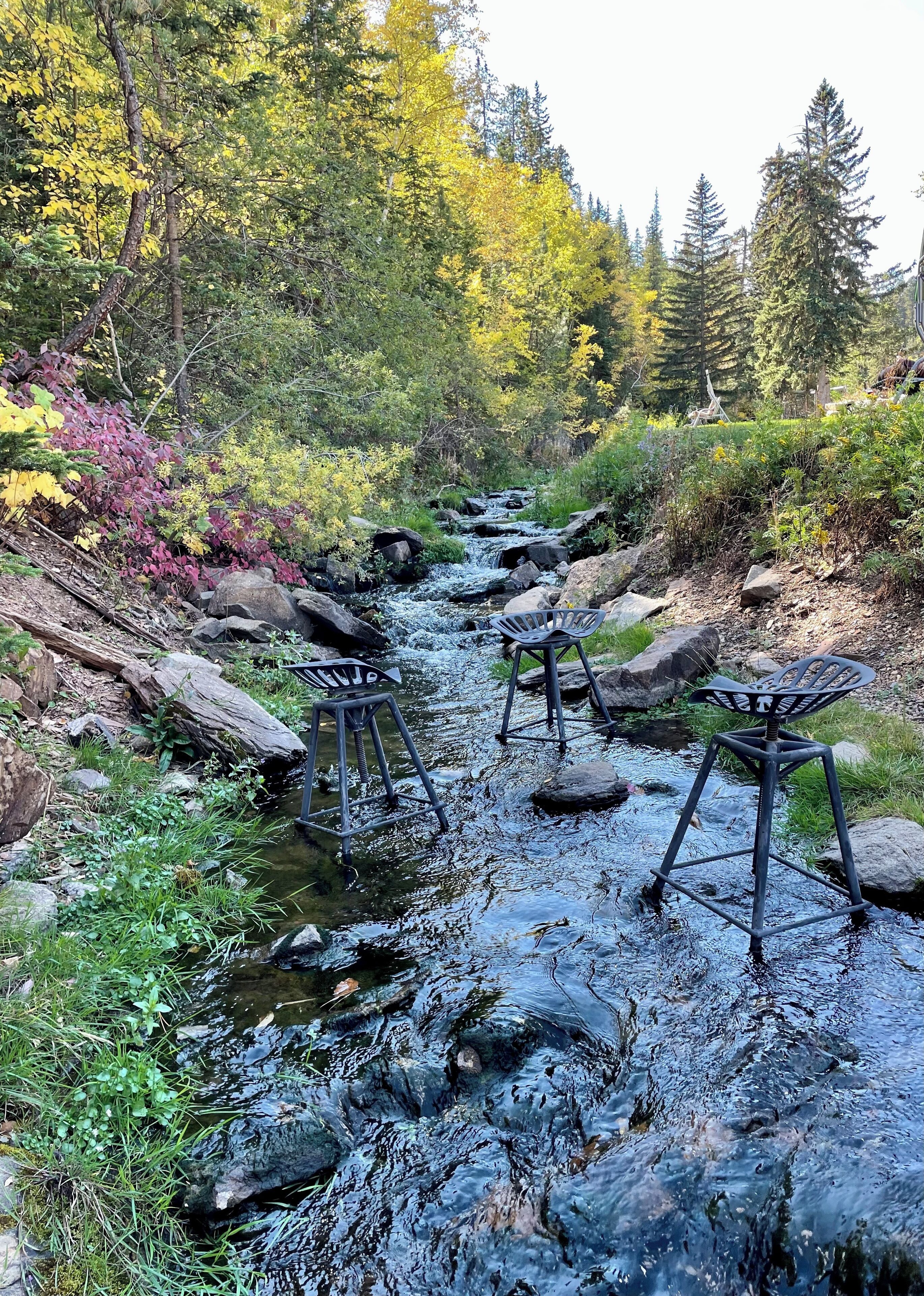 A natural outdoor setting with a stream, rocks, and chairs.