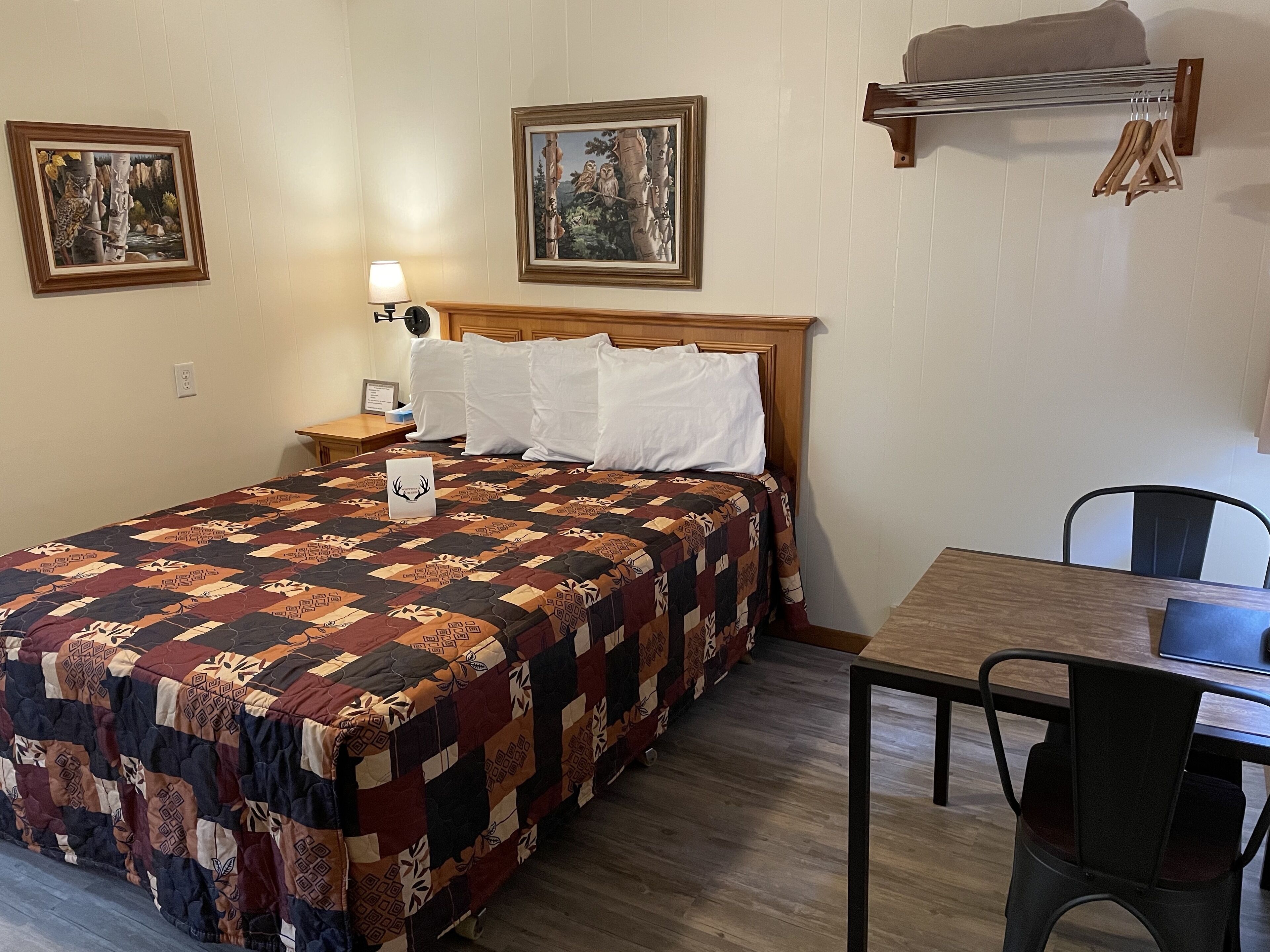 A neatly made bed with a patterned quilt, a bedside table with a lamp, and two framed pictures on the wall.