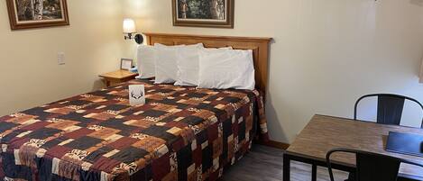 A neatly made bed with a patterned quilt, a bedside table with a lamp, and two framed pictures on the wall.