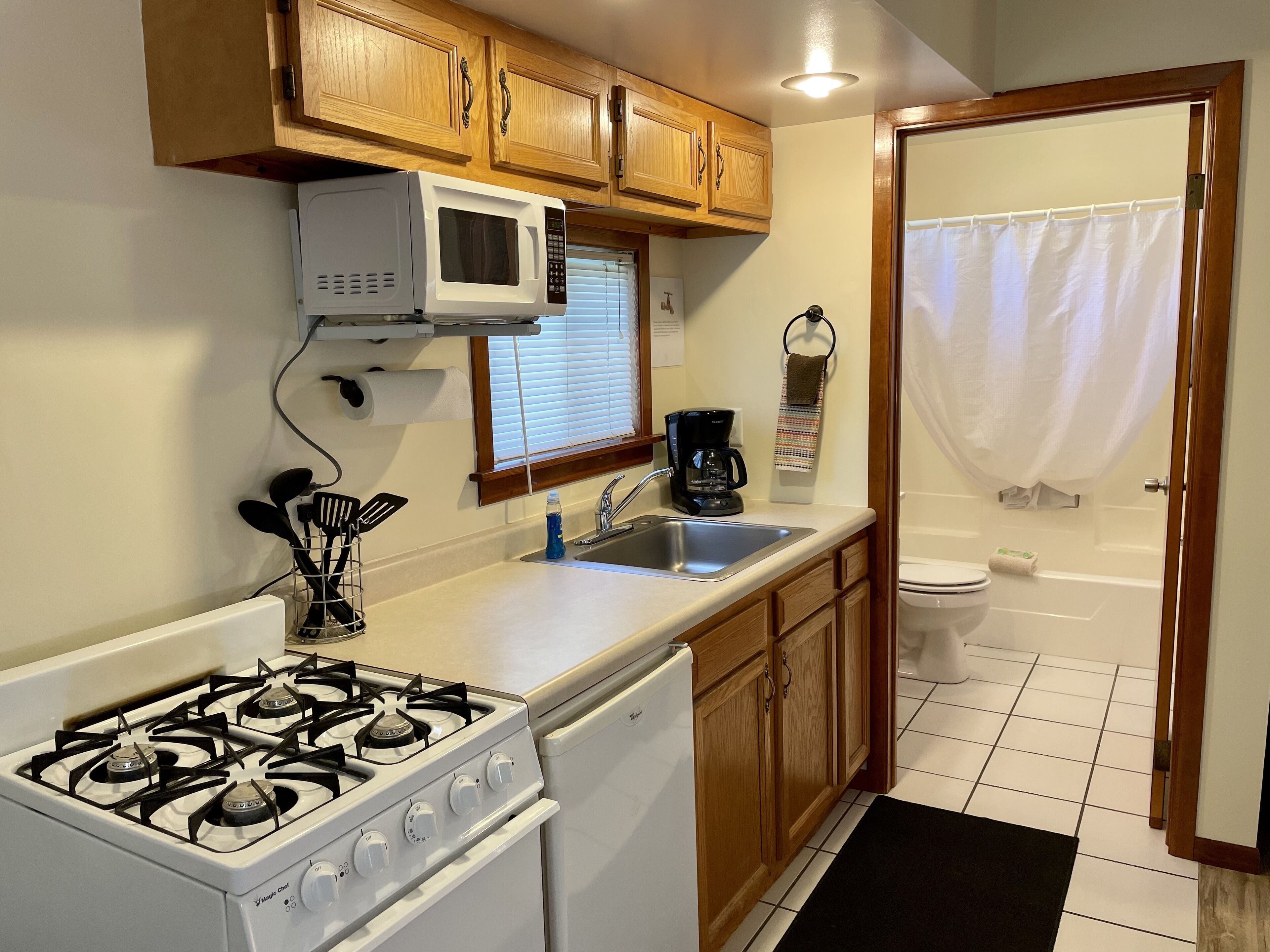 A compact kitchen with a stove, microwave, sink, and wooden cabinets.