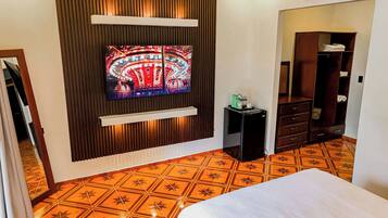 A hotel room with a television mounted on the wall, a minibar, a wardrobe, and a patterned floor.
