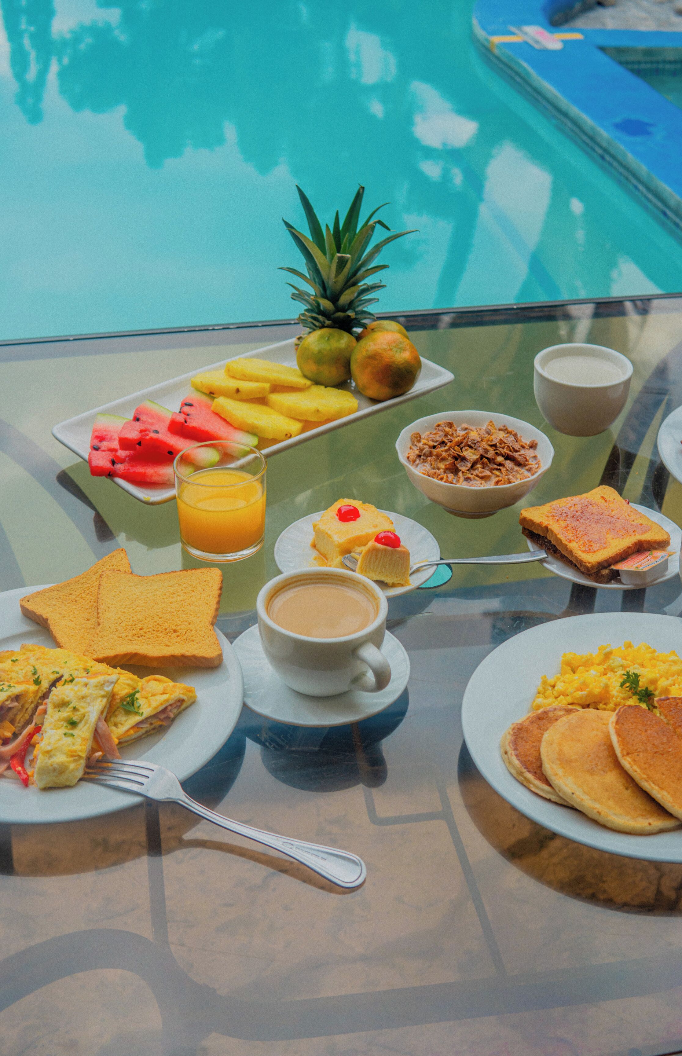 Ein Frühstücksbuffet mit verschiedenen Speisen und einem Glastisch in Poolnähe.