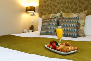 A neatly made bed with a green bedspread, a plate of strawberries and croissants, and a glass of orange juice on a hotel room. - Kingfisher Townhouse (Dublin)