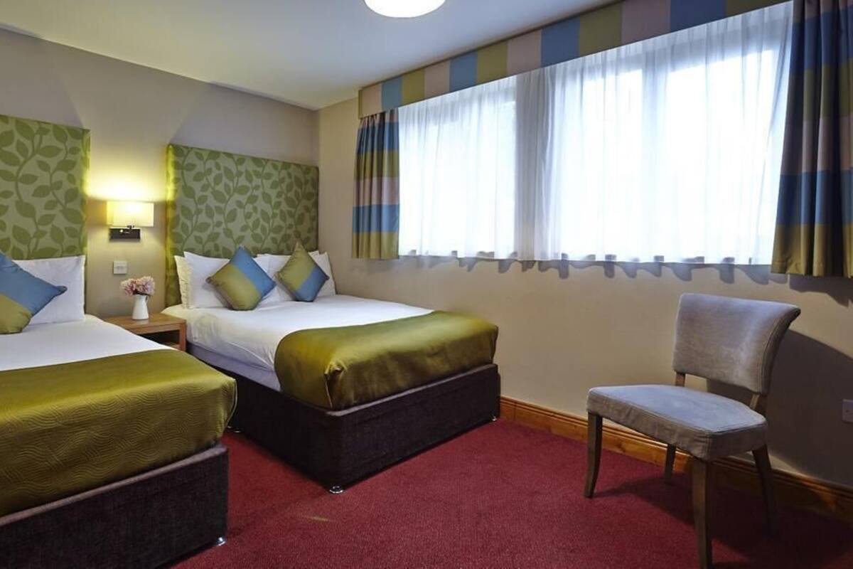 Una habitación de hotel con dos camas, una silla y una mesita de noche con lámpara.