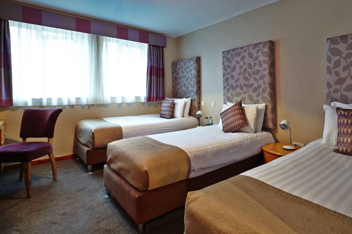Una habitación de hotel con dos camas, una silla y una mesita de noche con lámpara.