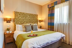 A neatly made bed with a green blanket, two pillows, and a bedside table with a lamp and a small plant. - Kingfisher Townhouse (Dublin)