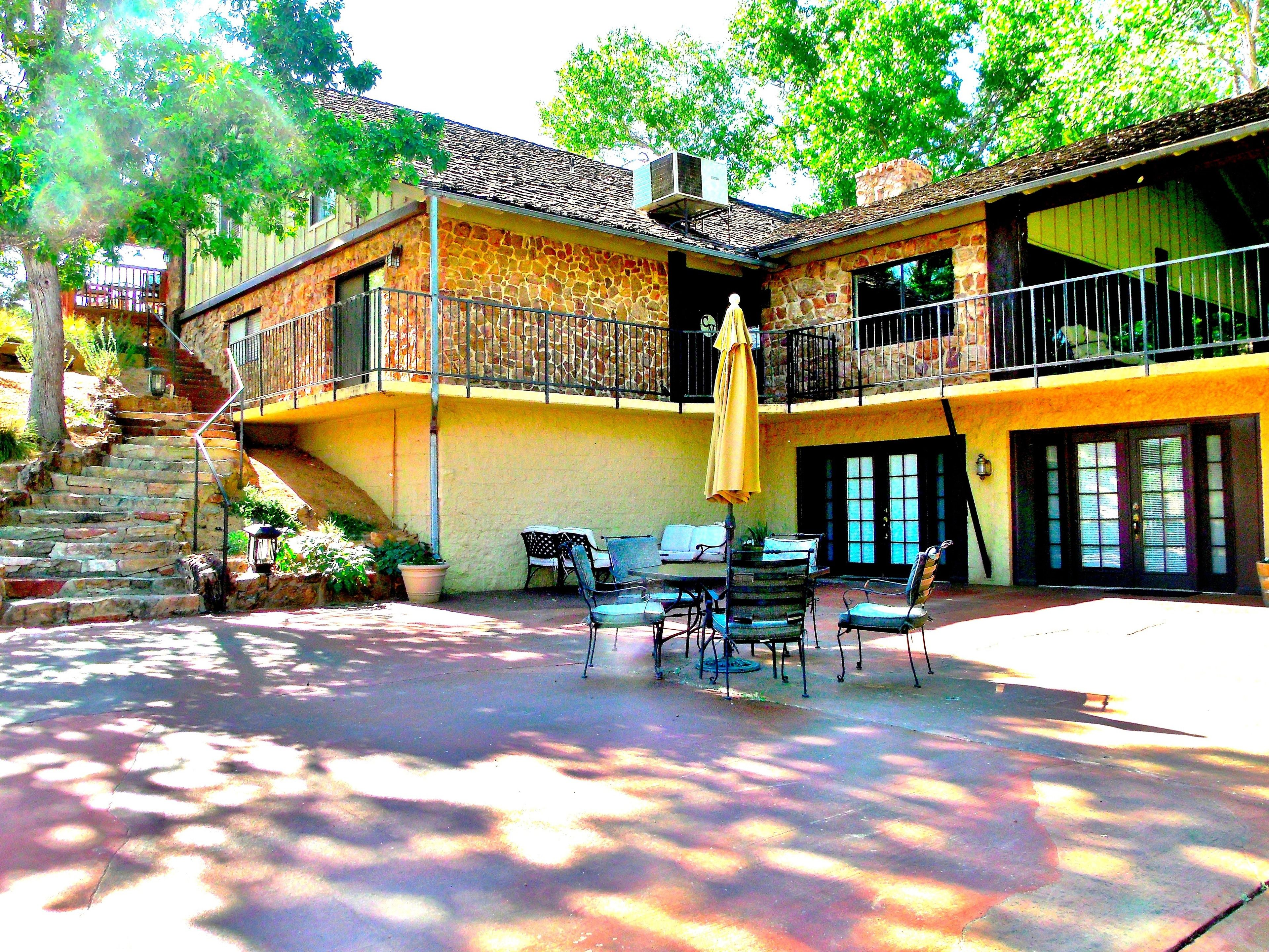 A two-story building with a stone facade, a balcony, outdoor seating area with chairs and a table, and a staircase leading to the upper level.