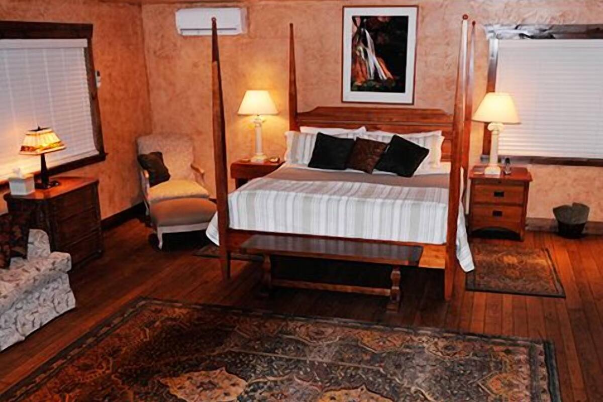 A bedroom with a wooden bed, two bedside tables with lamps, a chair, a rug, and a painting on the wall.