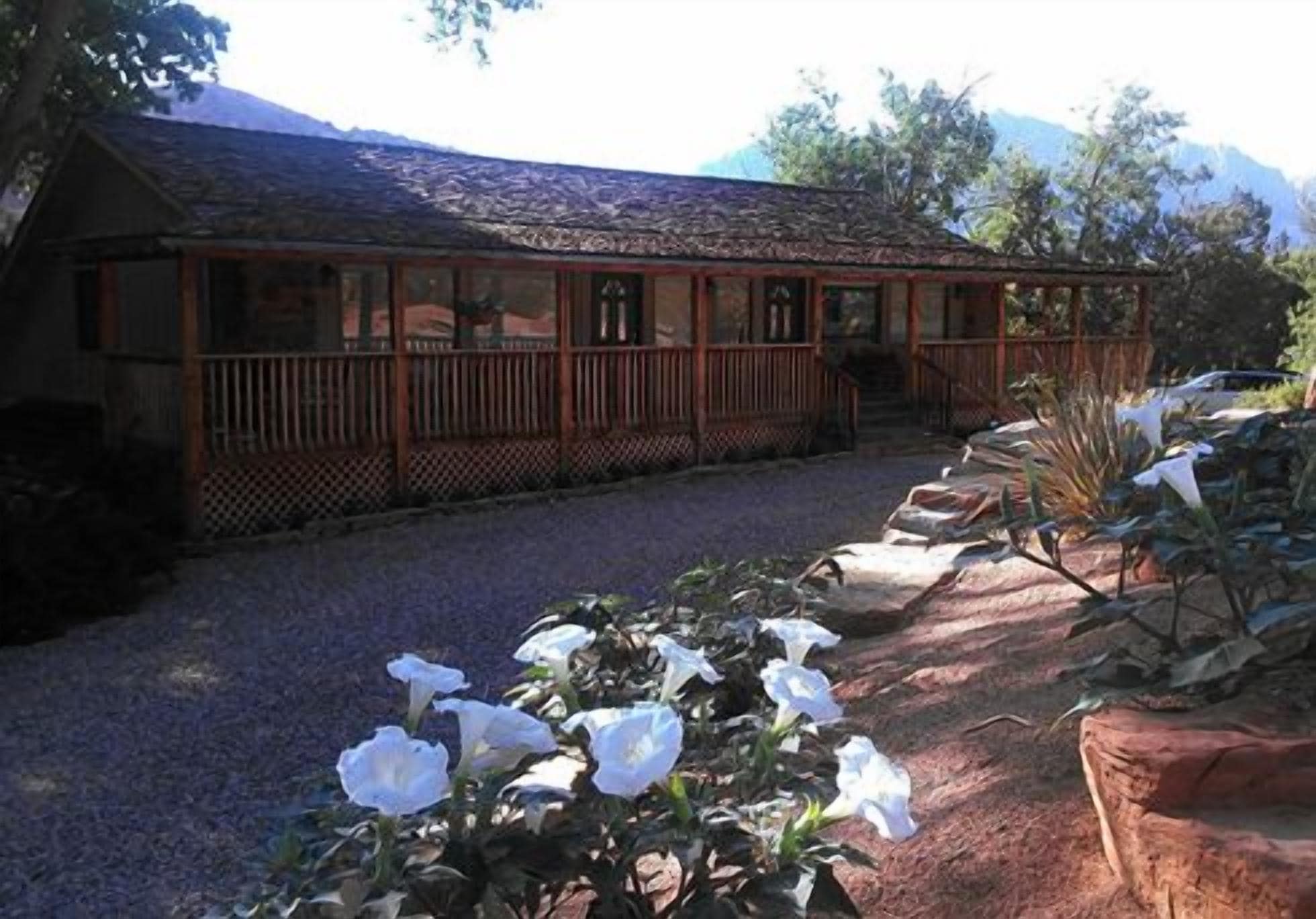 A wooden cabin with a porch, surrounded by gravel and plants.