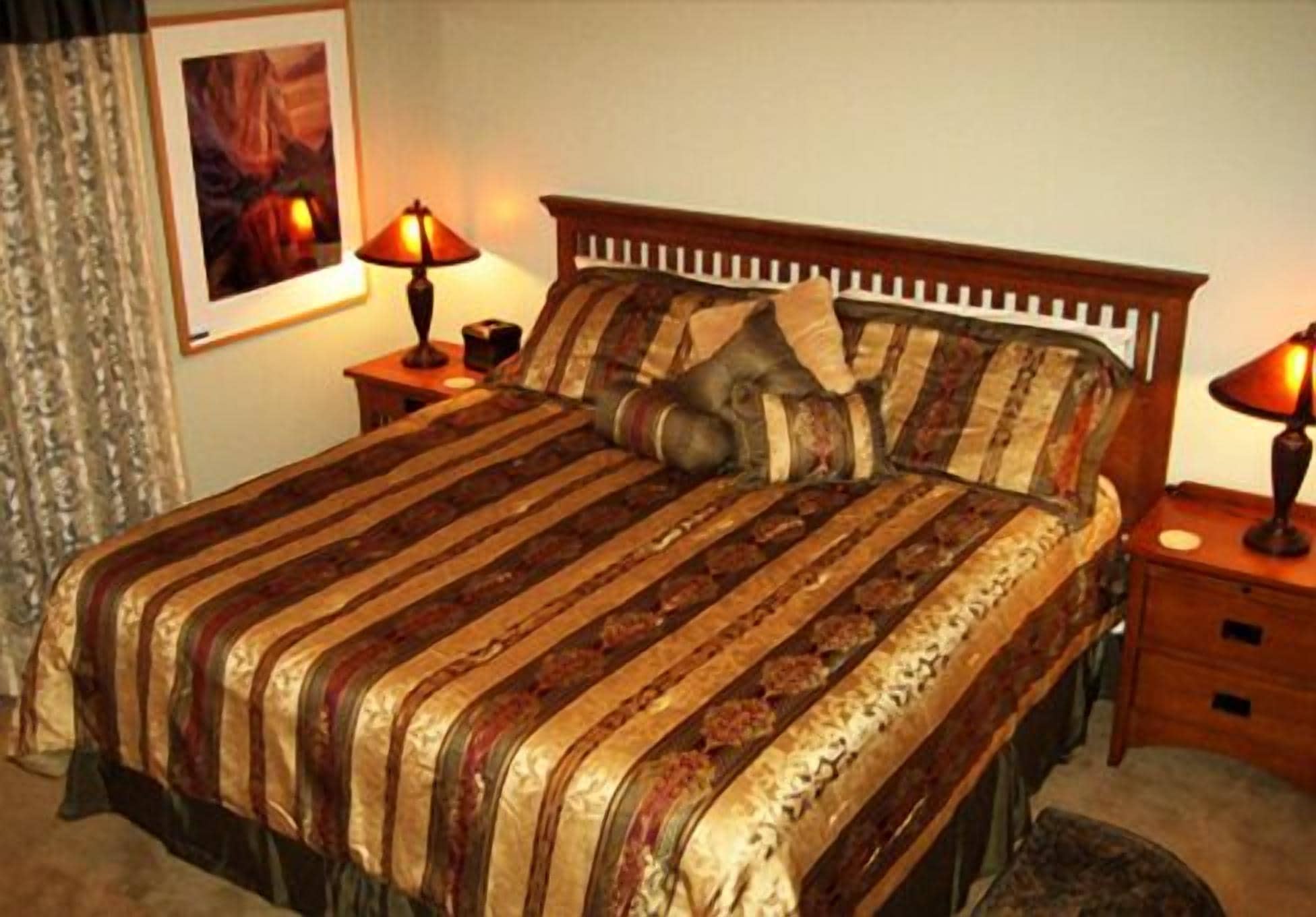 A neatly made bed with striped bedding and two bedside lamps.