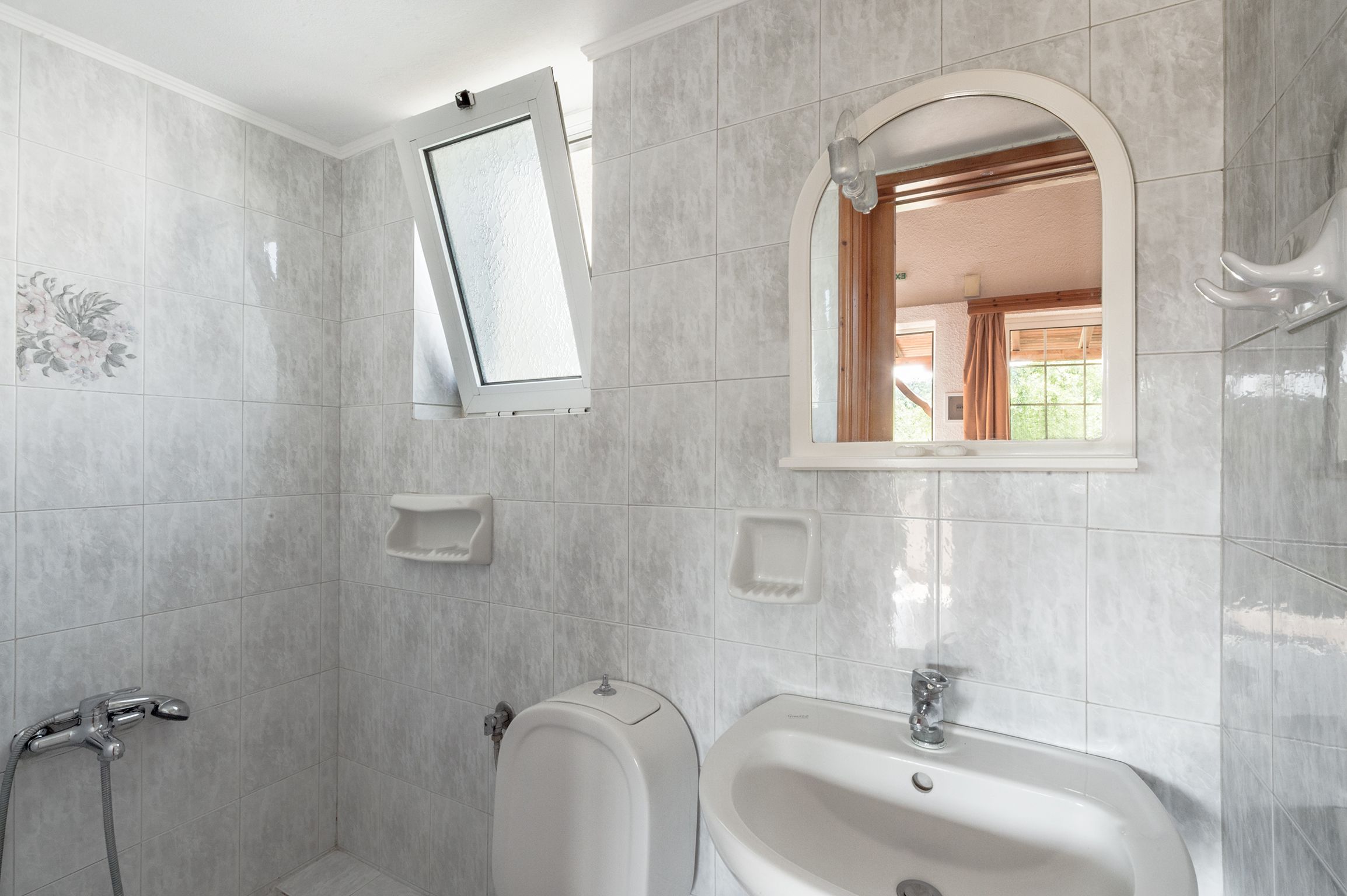 A bathroom with a shower, toilet, and sink, tiled in a light color.
