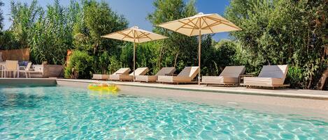 Una piscina cristalina con sillas de descanso y sombrillas, rodeada de follaje.