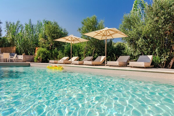 A clear swimming pool with lounge chairs and umbrellas, surrounded by greenery. - Koroni Village (Pylos-Nestoras)
