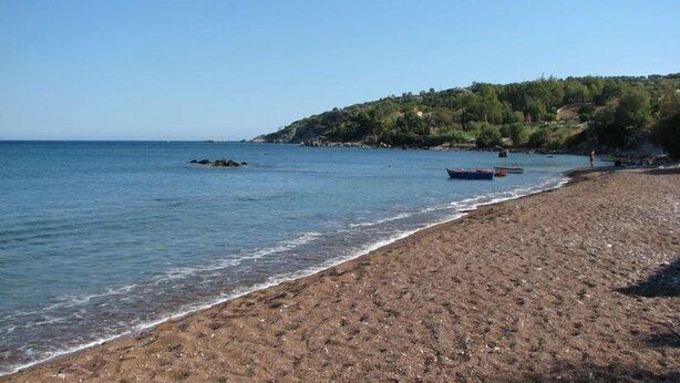 A beach with rocky terrain and a few boats in the water.