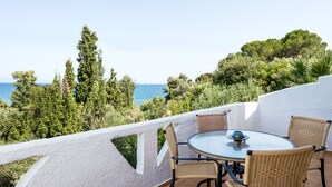 A terrace with a round table and wicker chairs overlooking a coastal landscape.