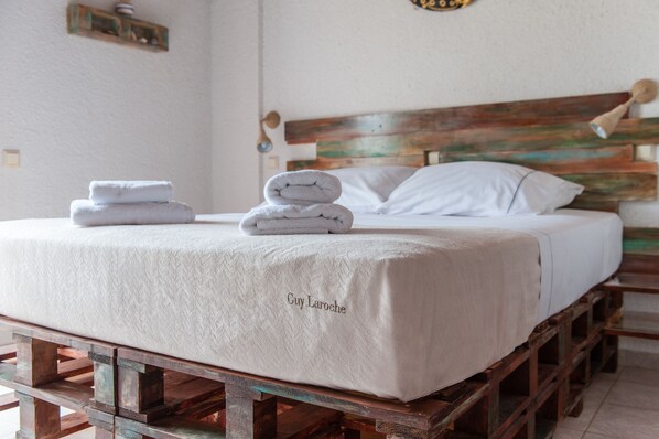 Una cama con una colcha blanca texturizada, una pila de toallas dobladas y un cabecero de madera.