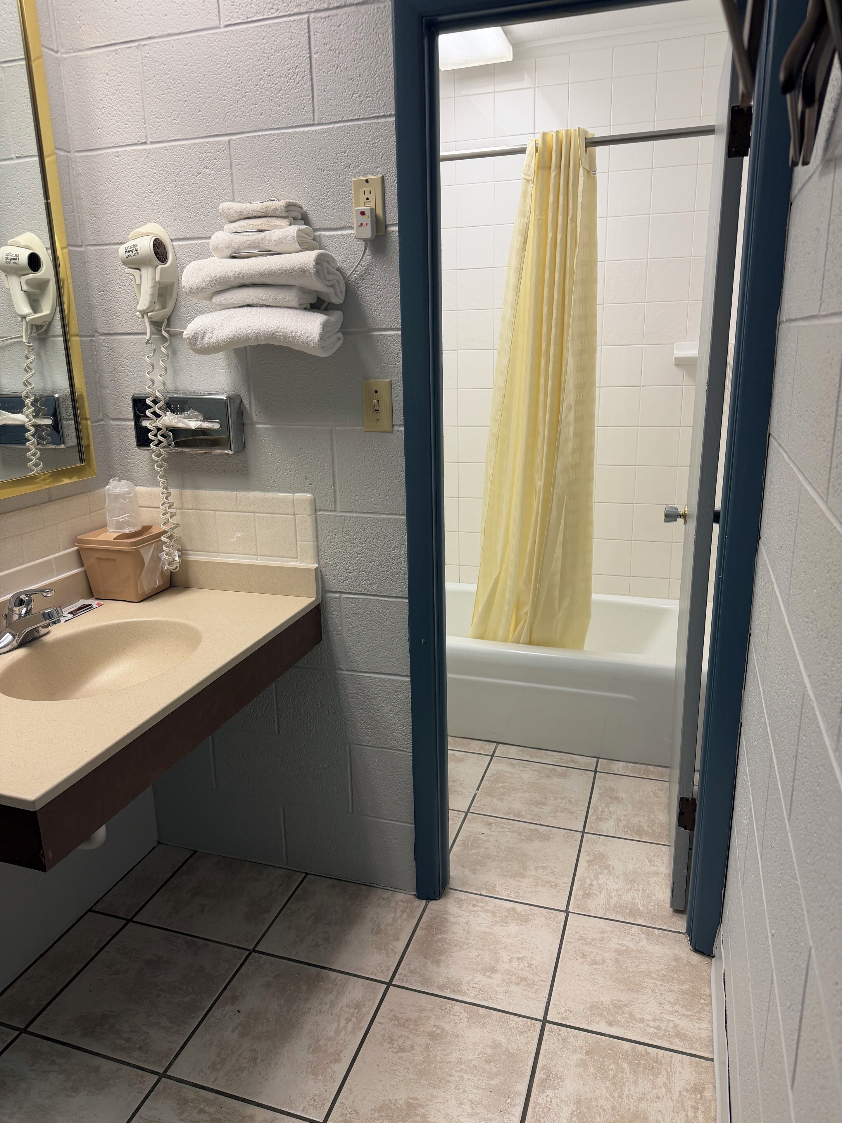 Une salle de bain équipée d’un lavabo, d’un miroir, d’un sèche-cheveux, d’un porte-serviettes et d’un rideau de douche.