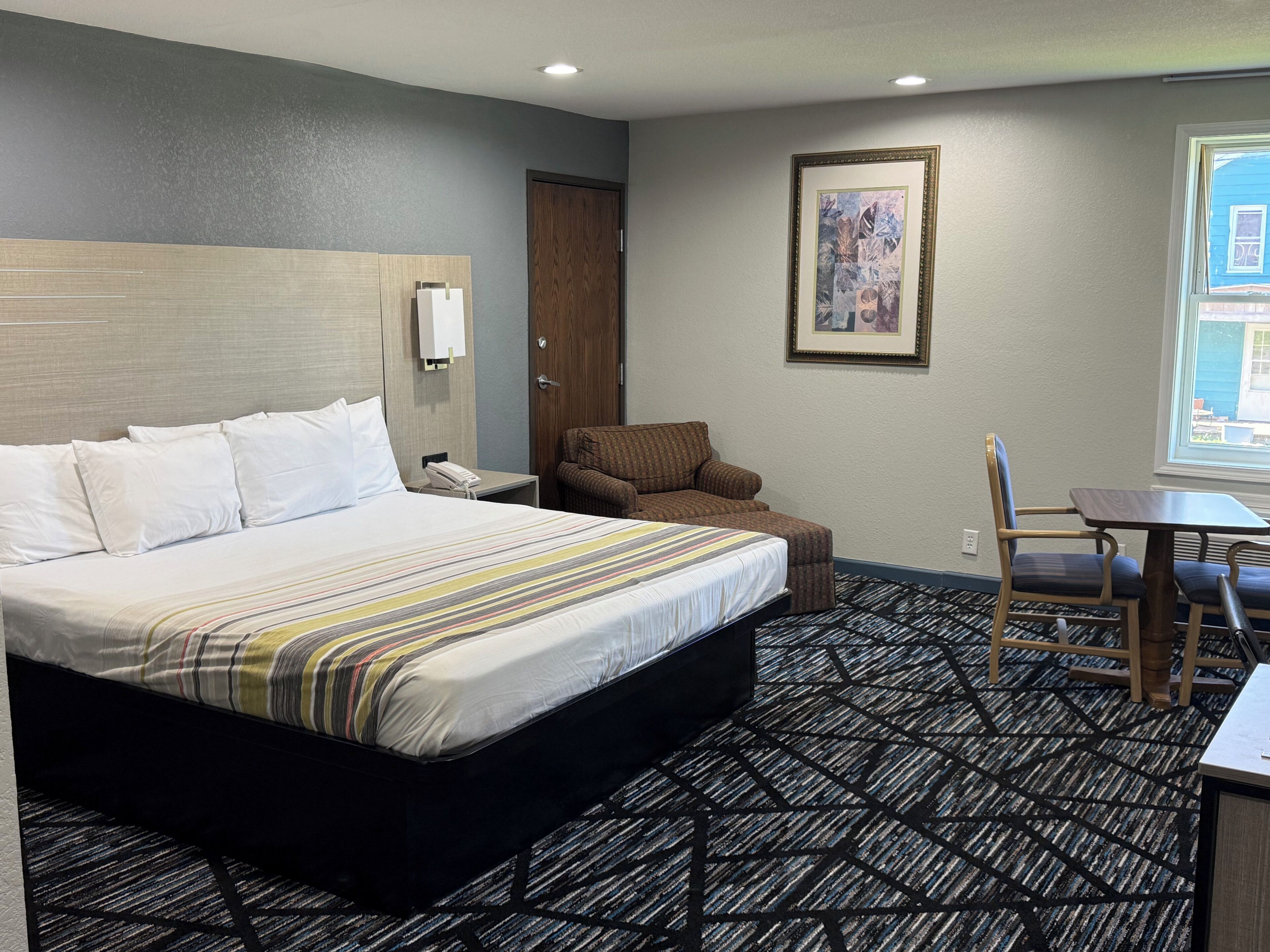 Een hotelkamer met een groot bed, een stoel, een klein tafeltje, een schilderij aan de muur en een raam.