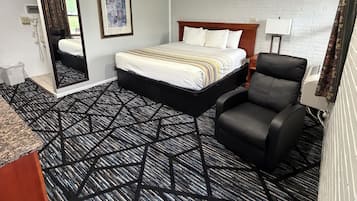 A hotel room with a bed, a chair, a desk, a mirror, and a picture on the wall.
