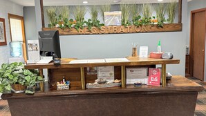 Taulell de recepció amb superfície de fusta, un monitor ViewSonic, un refrigerador d'aigua i un cartell amb els preus de les habitacions.