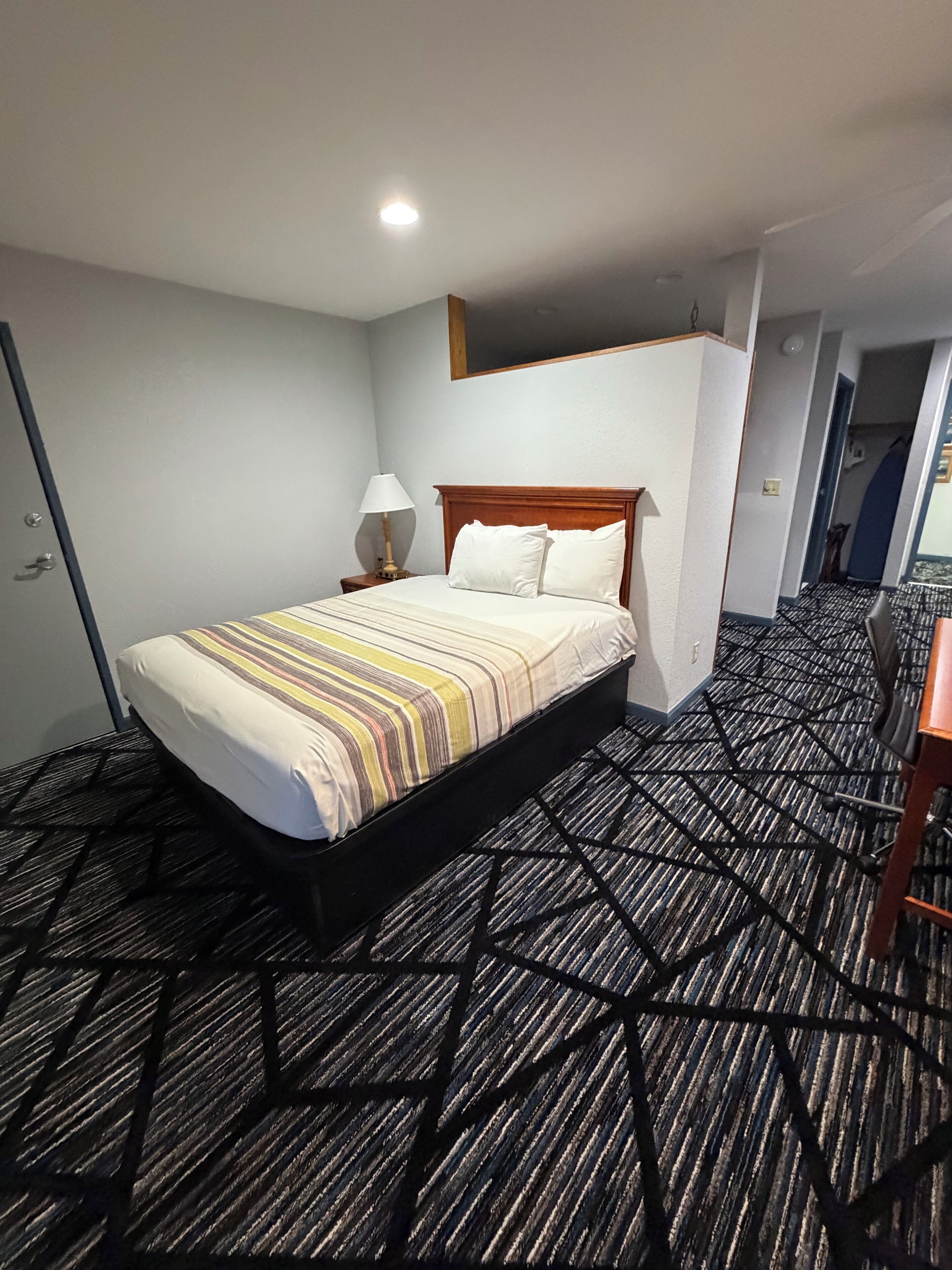 A hotel room with a bed, a nightstand, a lamp, and a carpeted floor.