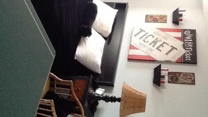 A bedroom with a bed, pillows, a ticket poster, a lamp, and a small wooden structure. - Hillside Cottages (Missouri Valley)