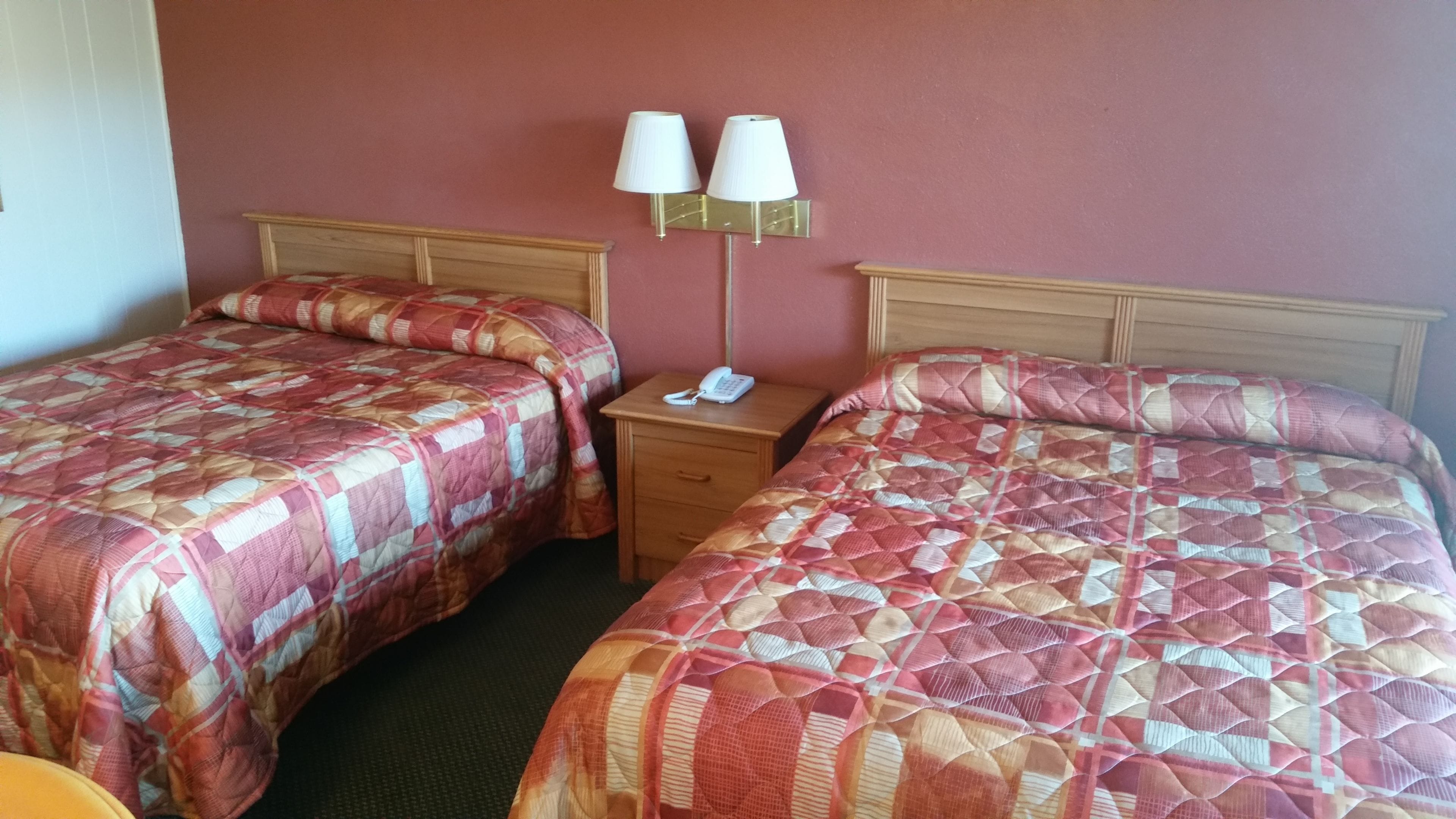 A hotel room with two beds, each with a patterned quilt, a bedside table with a lamp, and a phone.