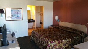 Quarto de hotel com cama, escrivaninha, cadeira, televisão, quadro, banheiro e luminária.
