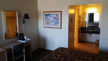 Habitación de hotel con cama, escritorio, lámpara, pintura y baño con lavamanos y espejo.