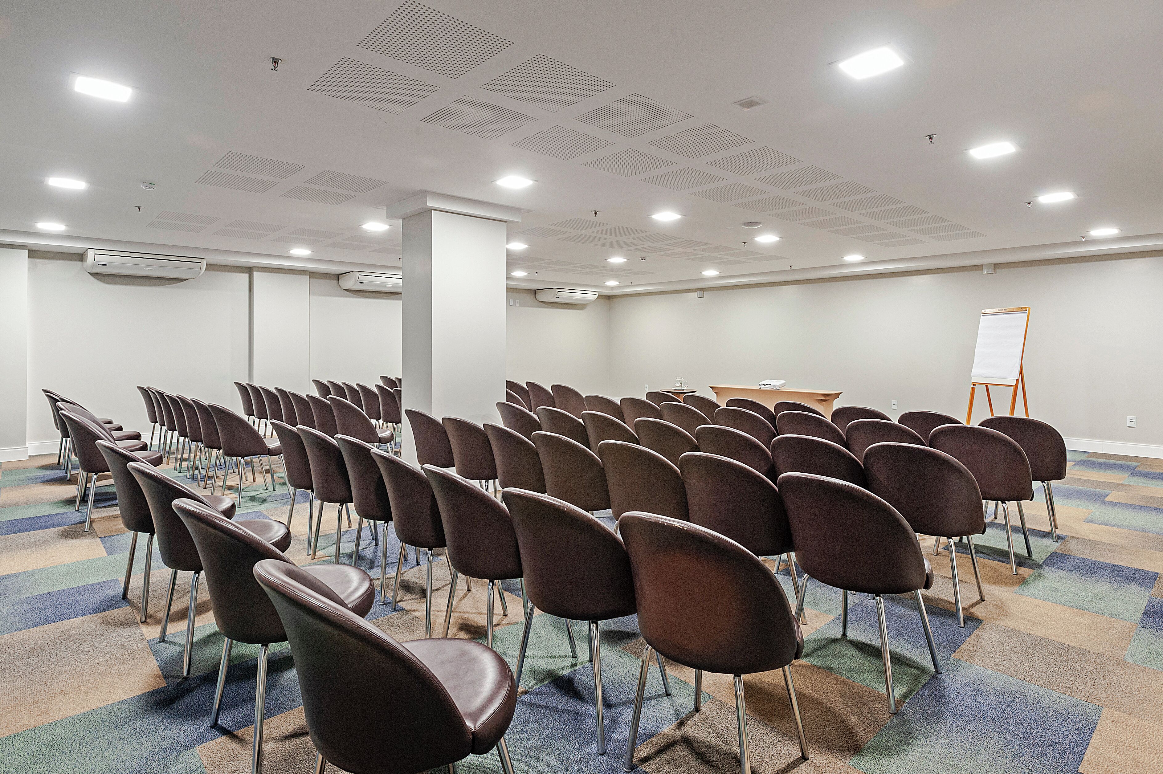 A conference room with rows of chairs, a whiteboard, and air conditioning units.