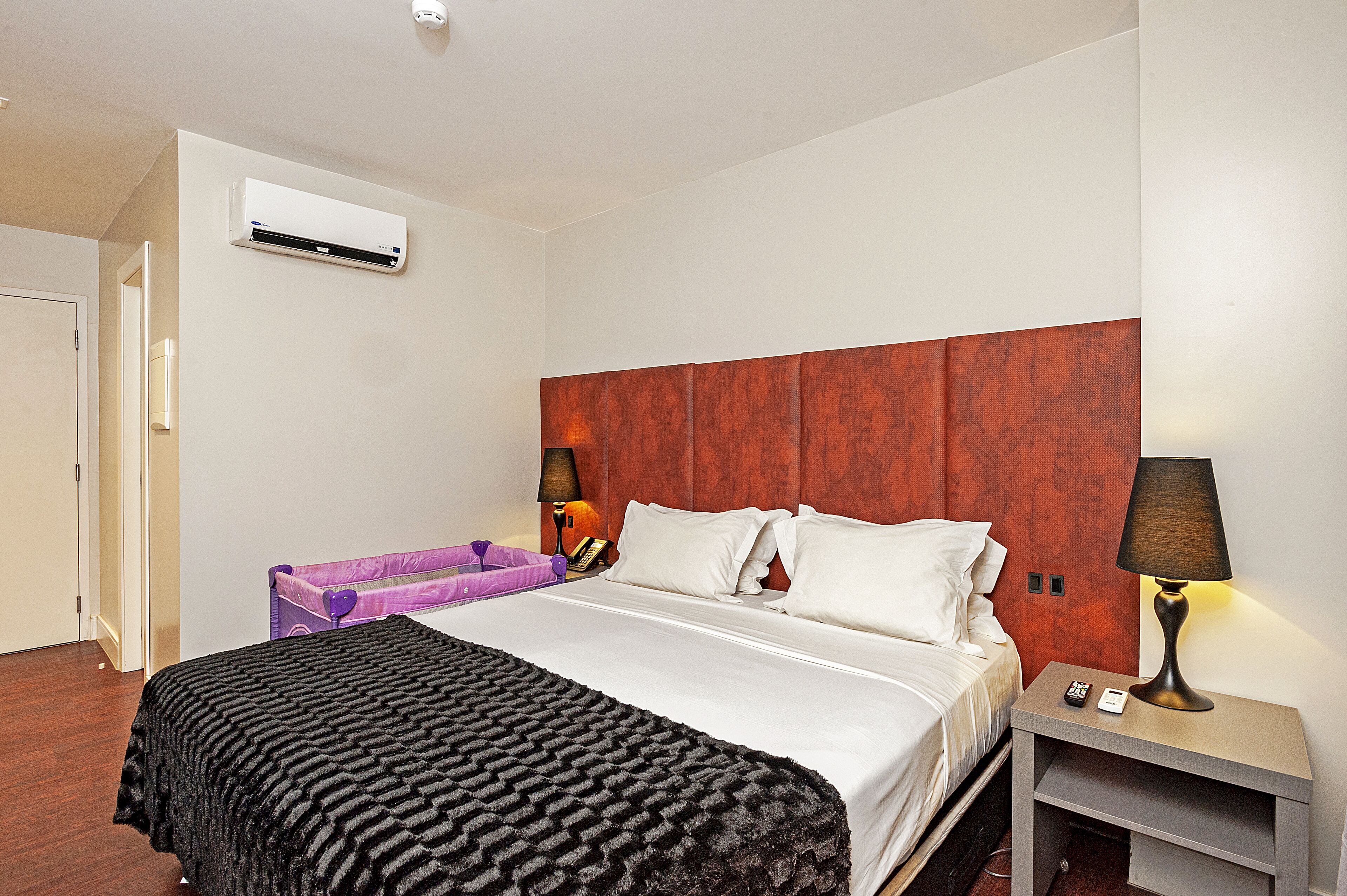 Ein Hotelzimmer mit Bett, Nachttisch, Lampe, Koffer und Klimaanlage.