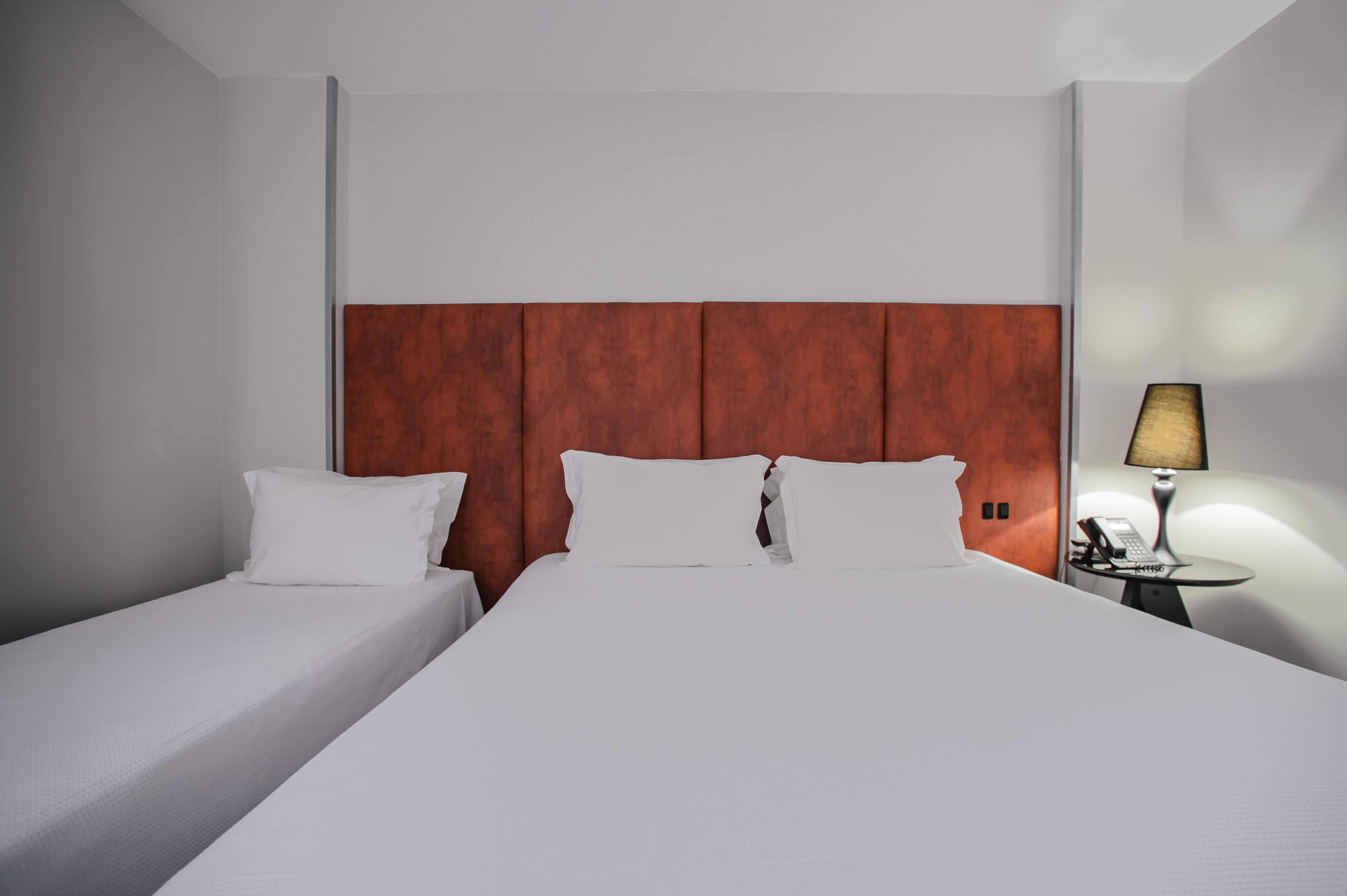 Een hotelkamer met twee enkele bedden, een houten hoofdbord, een nachtkastje met een lamp en een telefoon.